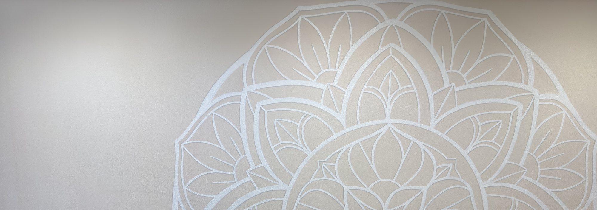 The hand-painted white mandala mural on the warm beige wall of the Vine Yoga studio